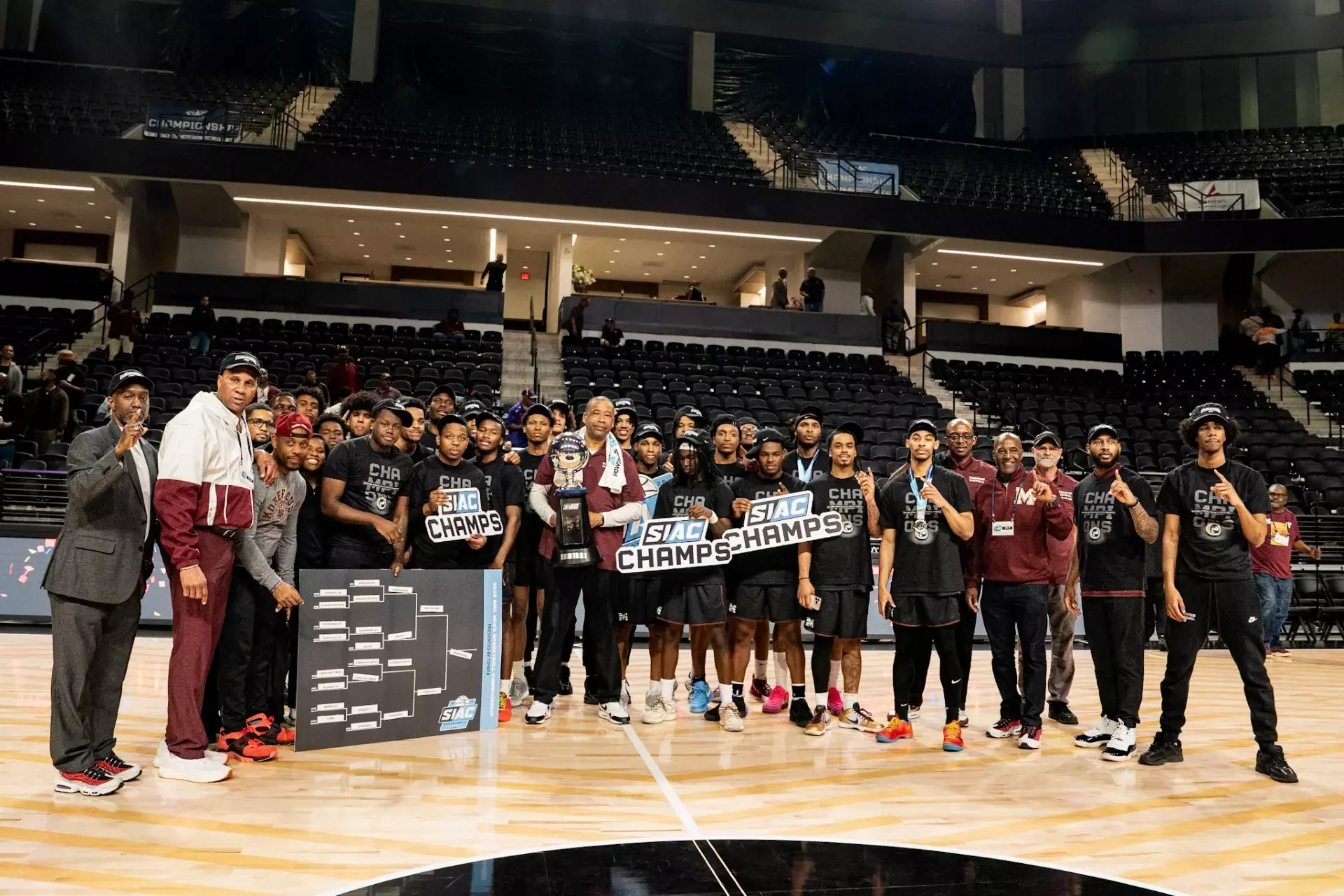 Morehouse basketball team and coaches on court holding the SIAC Championship trophy and CHAMPS signs