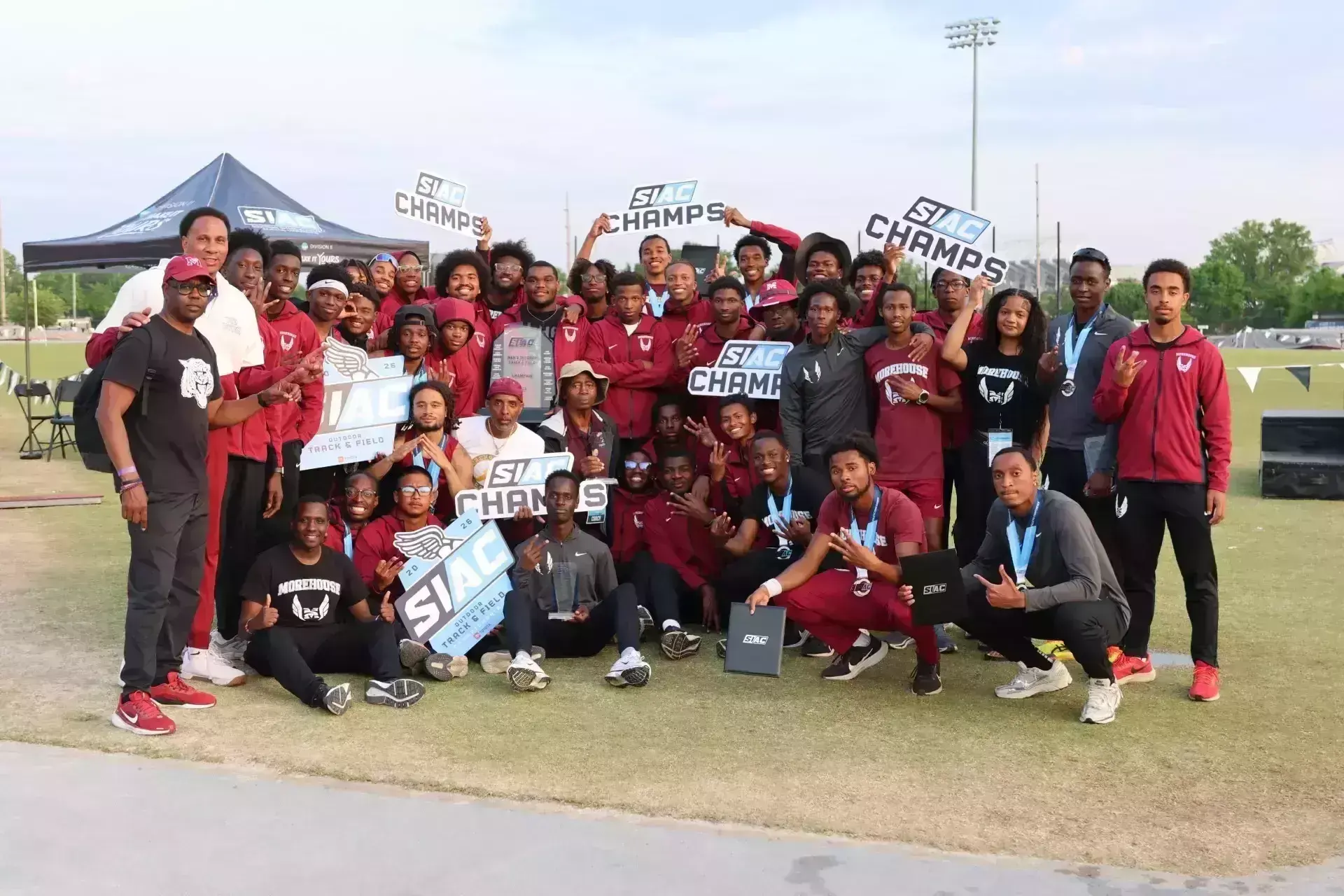 Morehouse outdoor track and field team celebrating on the field with SIAC Champs signs and the championship trophy
